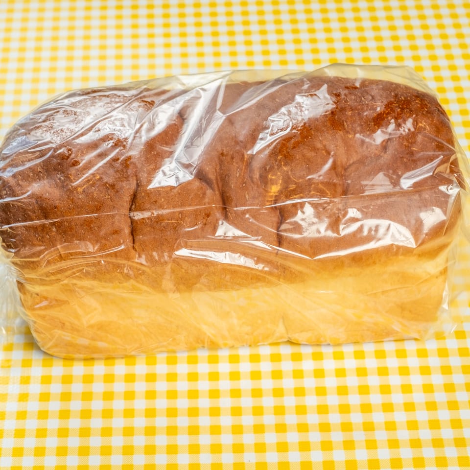 Loaf of sliced brown bread wrapped in clear plastic on a yellow-and-white checkered tablecloth.