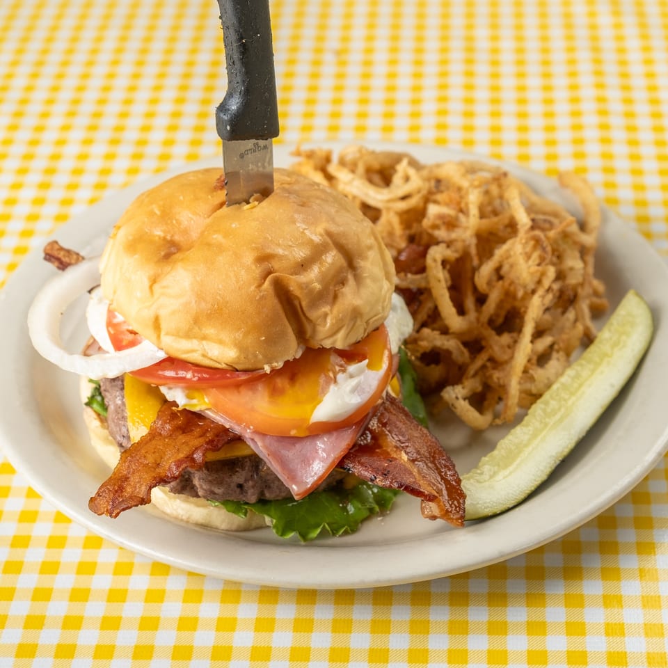 Bacon cheeseburger with lettuce, tomato, onion, and sauce served with crispy fried onions and a pickle spear.