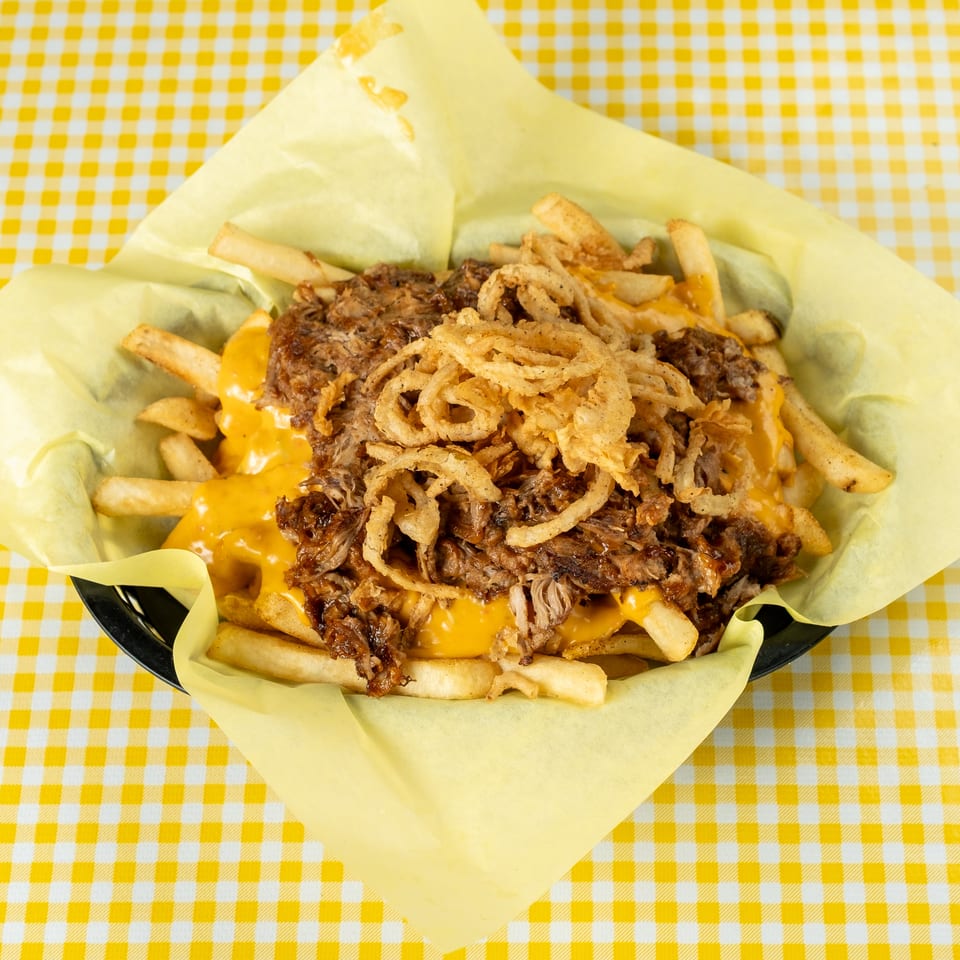 Loaded fries topped with pulled beef, melted cheddar cheese, and crispy fried onions on a yellow checkered tablecloth.